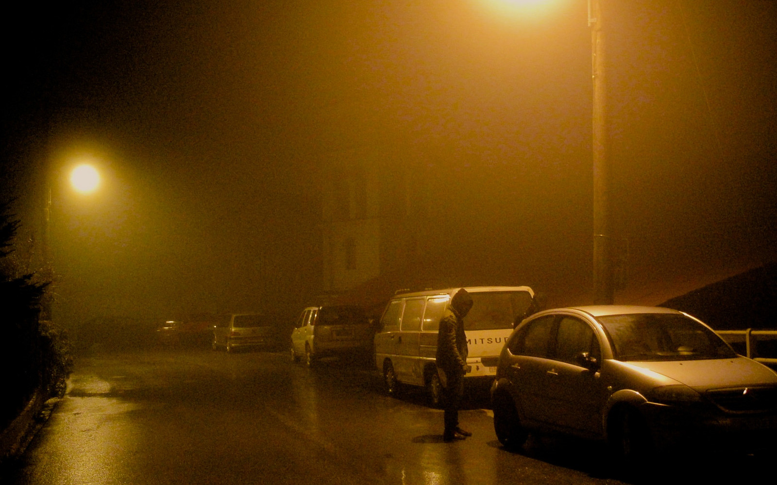 Image: A foggy/rainy city street with hooded individuals around a car.