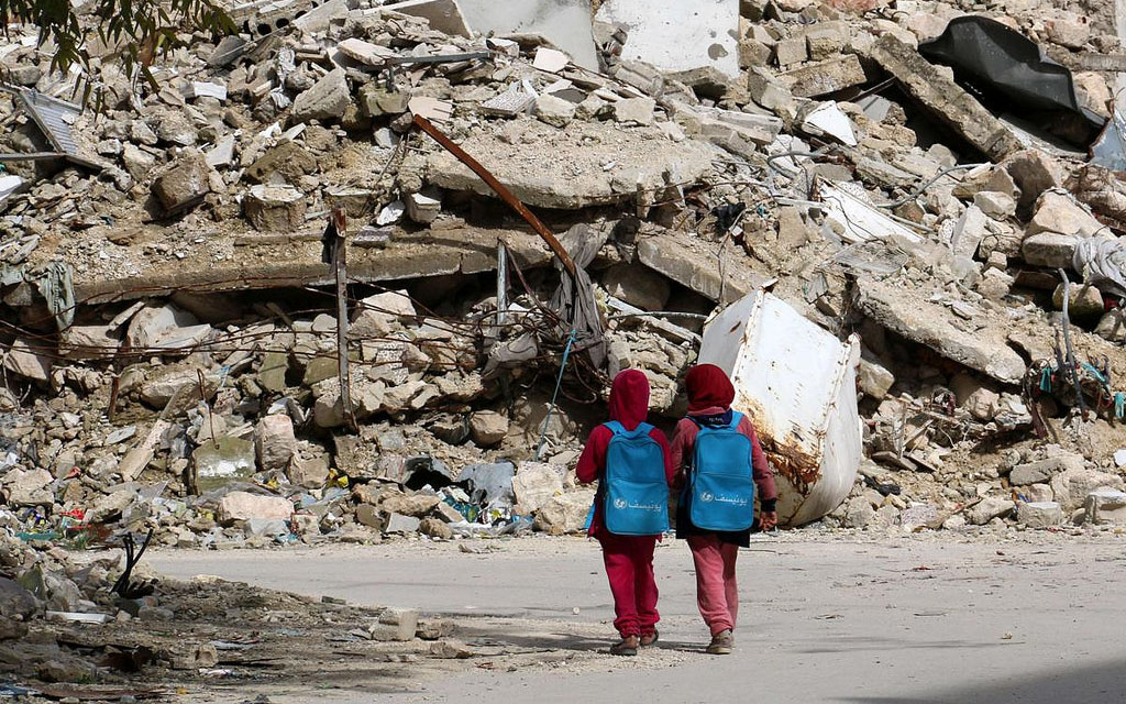 Image: Two young children walking in the rubble of a city.
