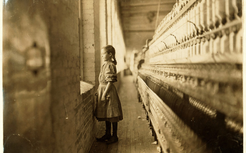 Image: A young girl staring out a window at a brick wall.