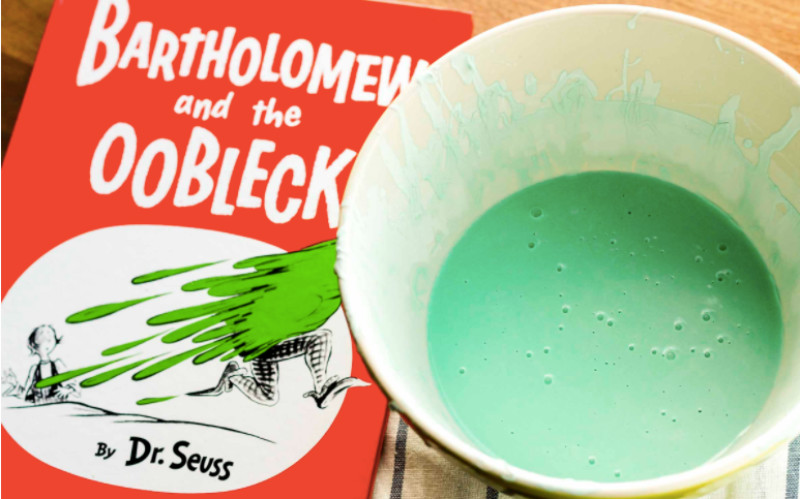 Image: A cup of green oobleck next to Bartholomew and the Oobleck by Dr. Seuss