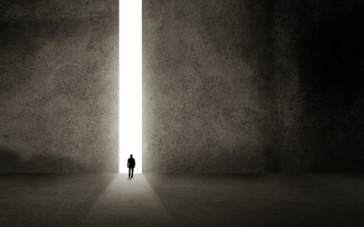 Image: A man walking through a narrow opening of light out of darkness.