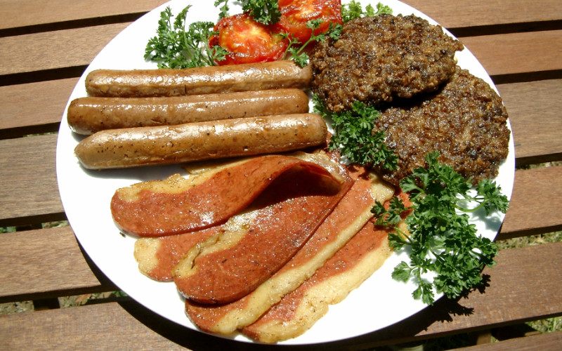 Image: A plate of vegan meat replacement, including sausage, patties, and other meats.