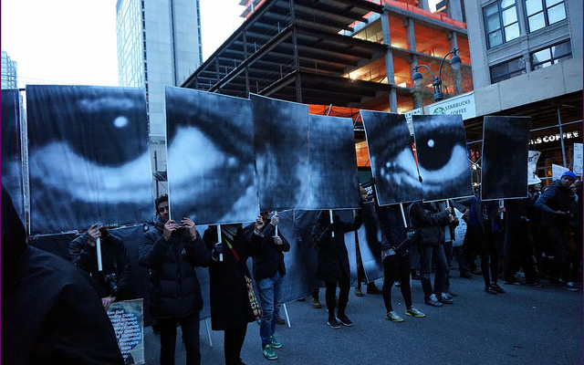 Image: A picture of protesters holding up signs that create a composite image of a face.