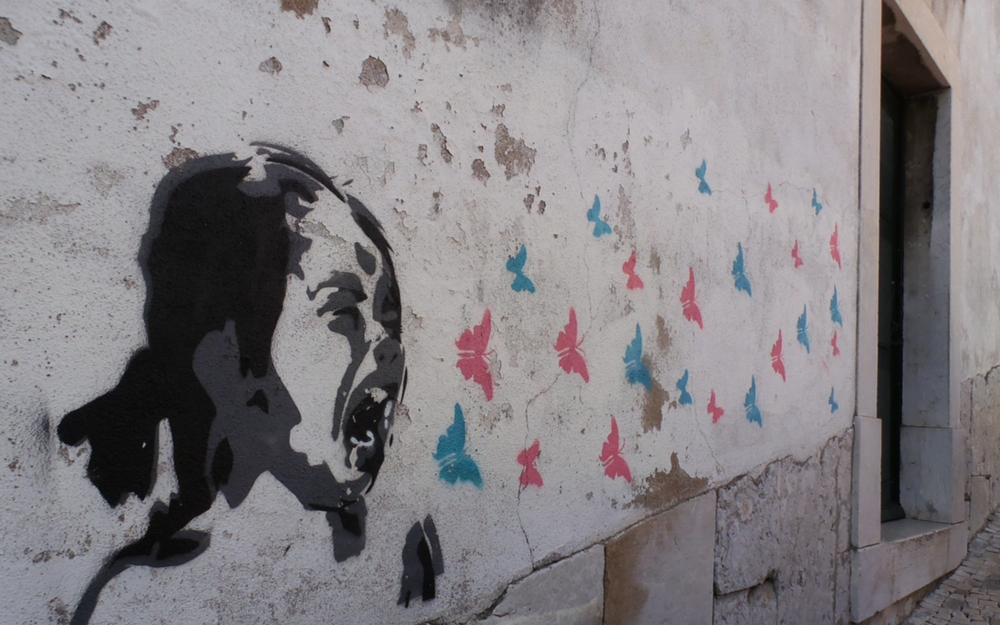 Image: A photo of street art where a young girl screams and blue and pink butterflies flutter out of her mouth