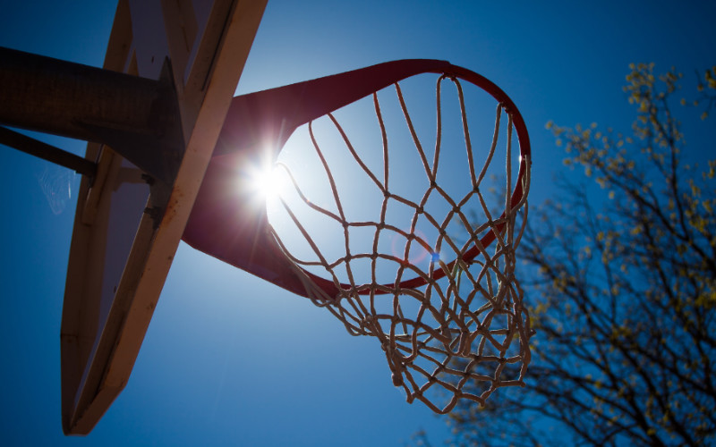 Image: Sun barely shining through a basketball hoop.