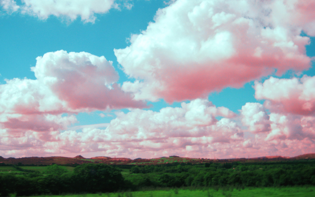 Image: Slightly pinkish clouds over a green landscape with hills.