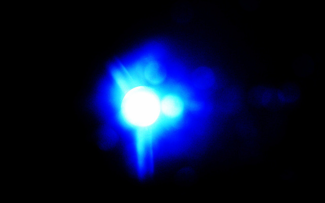 Image: An abstract blue light with water spots surrounded by blackness.